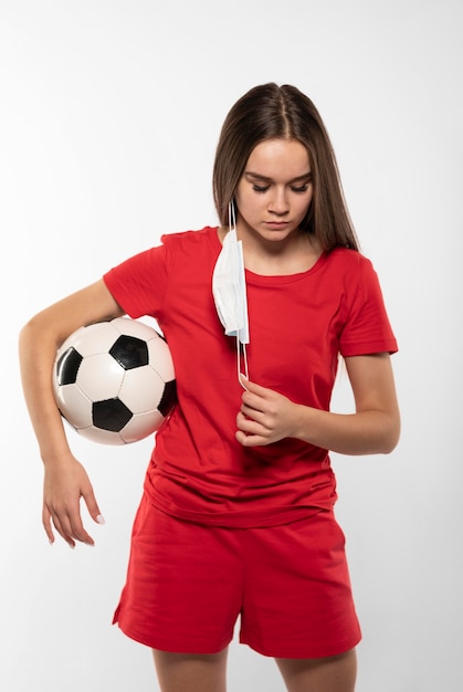 Jogador de futebol feminino com máscara segurando uma bola