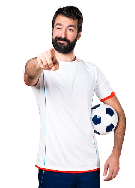 Jogador de futebol segurando uma bola de futebol apontando para a frente