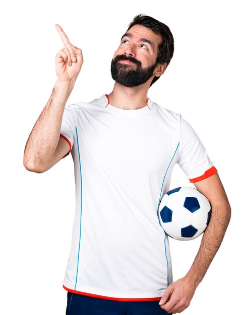 Jogador de futebol segurando uma bola de futebol apontando para cima