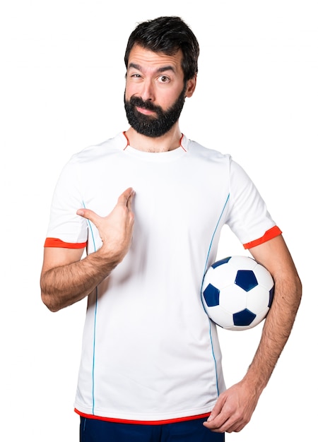 Jogador de futebol segurando uma bola de futebol fazendo um gesto de surpresa