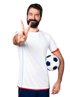Jogador de futebol segurando uma bola de futebol fazendo um gesto de vitória