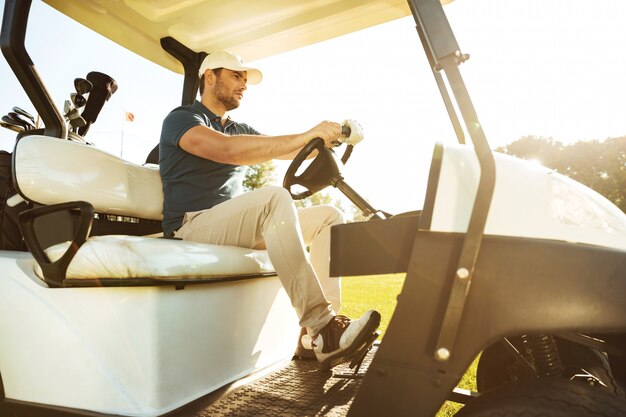 Jogador de golfe masculino dirigindo um carrinho com tacos de golfe