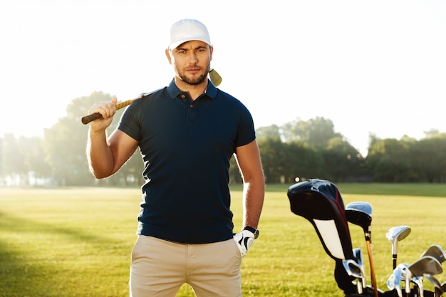Jogador de golfe masculino seguro considerável que está com clube de golfe