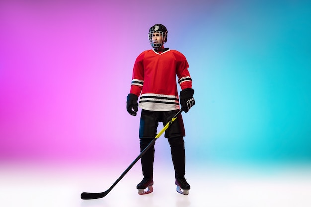 Foto grátis jogador de hóquei com o taco posando na quadra de gelo e uma parede gradiente de cor neon