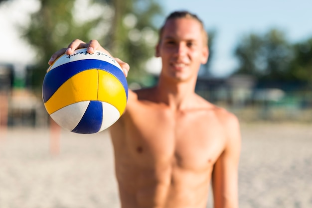 Jogador de voleibol masculino sem camisa desfocado na praia segurando uma bola