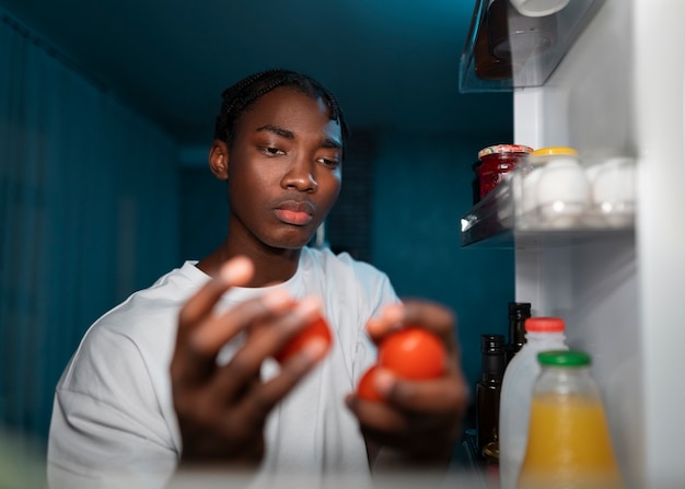 Jovem abrindo a geladeira em casa para um lanche no meio da noite