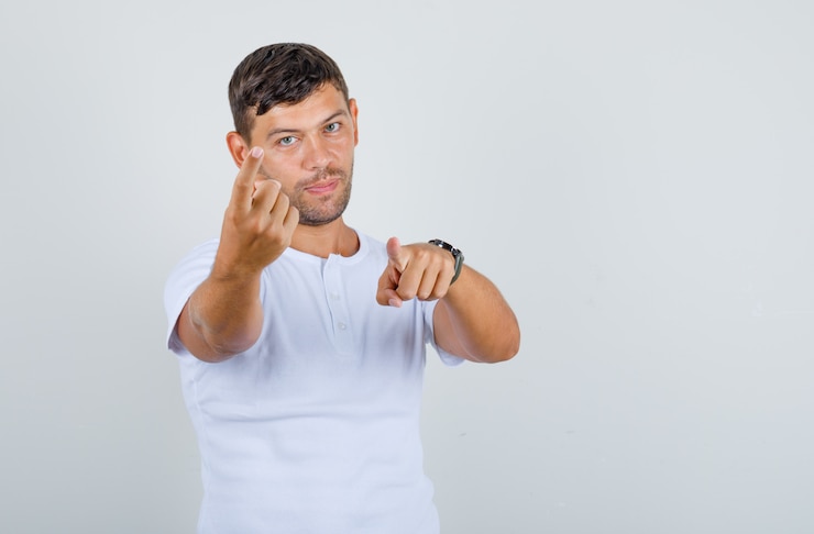 Foto grátis jovem acenando e apontando o dedo para a câmera em uma camiseta branca e olhando a vista frontal positiva.