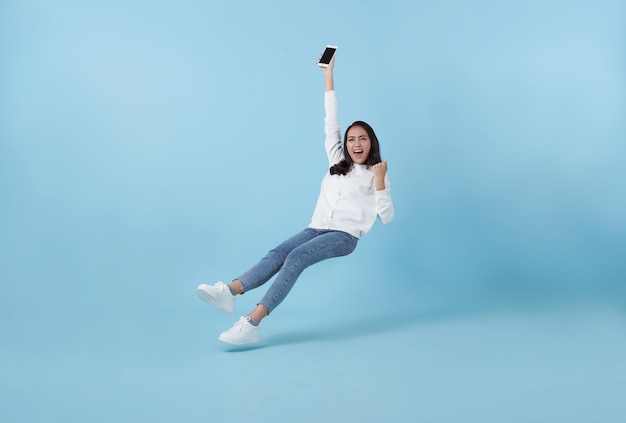 Jovem adolescente asiática feliz de mão segurando celular flutuando no ar isolada em fundo azul conceito de internet rápida