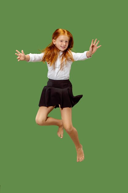 Jovem adolescente caucasiana feliz pulando no ar, isolado no fundo verde do estúdio.