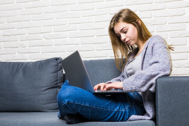 Jovem adolescente sentada no quarto da cama em casa, trabalhando no laptop, escrevendo cartas, navegando na internet em casa