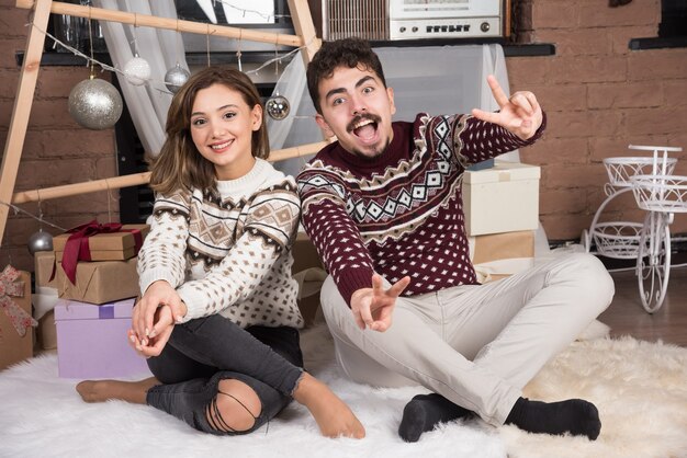 Jovem adorável casal sorridente, sentado no chão e posando.