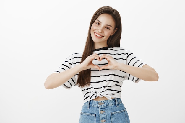 Jovem adorável e adorável mostrando gesto de coração e sorrindo, confessa simpatia ou amor