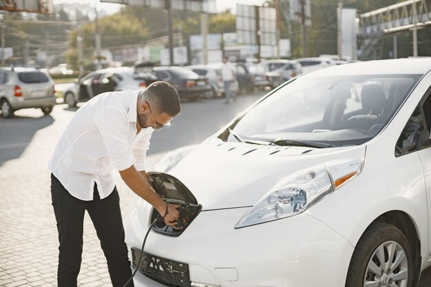 Jovem adulto carregando seu carro elétrico na cidade. Conceito de carro elétrico ecológico.