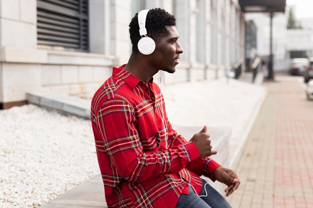 Jovem adulto de camisa vermelha ouvindo música, vista lateral