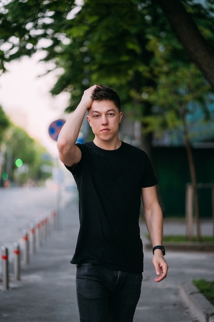 Jovem adulto em uma camiseta preta e jeans caminha em uma rua da cidade em um dia ensolarado