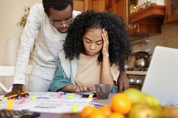 Foto grátis jovem africana intrigada com dor de cabeça enquanto calculava o orçamento familiar na mesa da cozinha