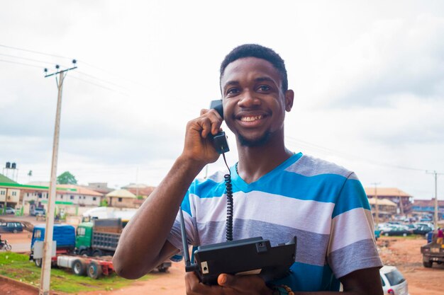 Jovem africano bonito vestindo pano de tira sorrindo enquanto ele está fazendo uma ligação com seu telefone terrestre