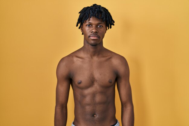 Jovem africano com dreadlocks em pé sem camisa relaxado com expressão séria no rosto. olhar simples e natural para a câmera.