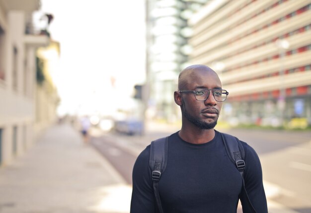 Jovem africano do sexo masculino com óculos, vestindo uma camiseta preta e uma mochila na rua