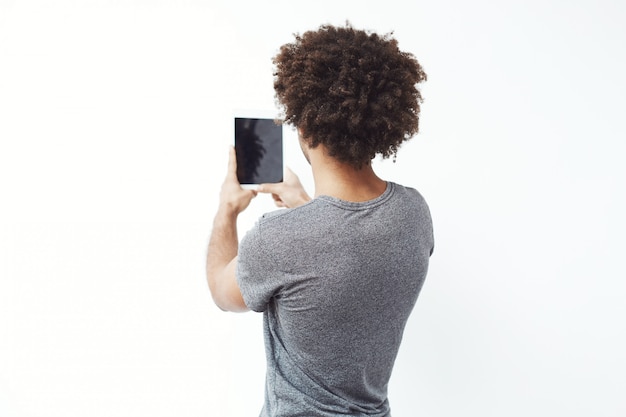 Jovem Africano em pé de volta para a câmera, olhando para o tablet.