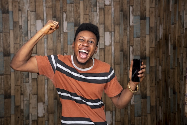 Jovem africano ficando animado com o telefone enquanto o segura com alegria
