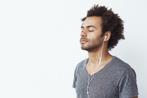 Jovem Africano ouvindo música em fones de ouvido com os olhos fechados.