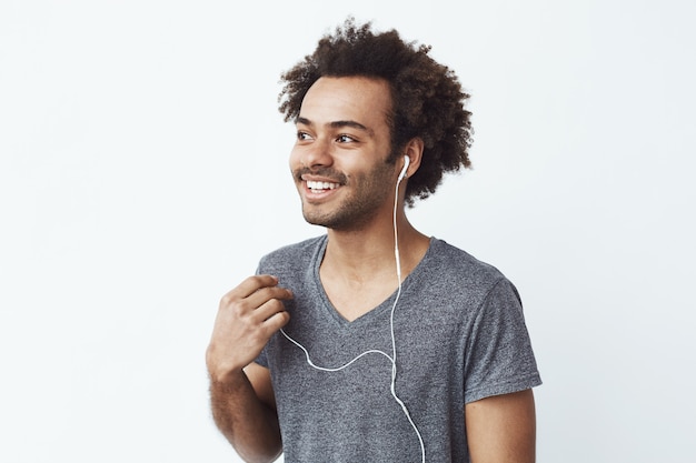 Jovem africano sorrindo apagando um fone de ouvido com fio sobre parede branca, ouvindo os pássaros.