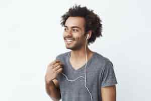 Foto grátis jovem africano sorrindo apagando um fone de ouvido com fio sobre parede branca, ouvindo os pássaros.