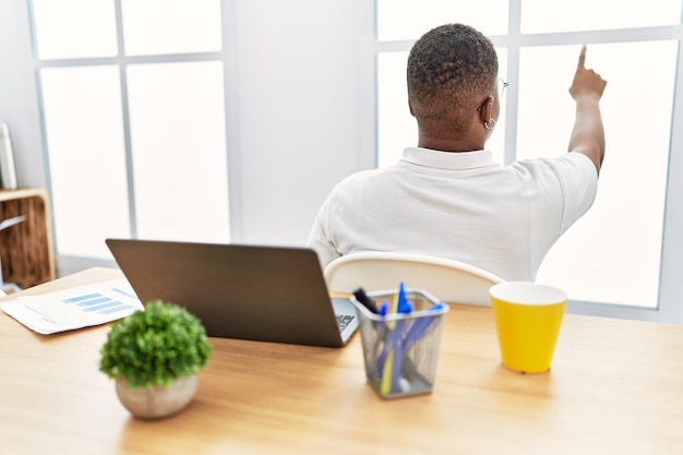 Foto grátis jovem africano trabalhando no escritório usando computador laptop posando para trás apontando para a frente com a mão do dedo