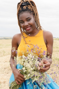 Jovem afro-americana se divertindo ao ar livre ao pôr do sol. garota rindo em campo. buquê de flores silvestres. bela jovem afro-americana com rabo de cavalo