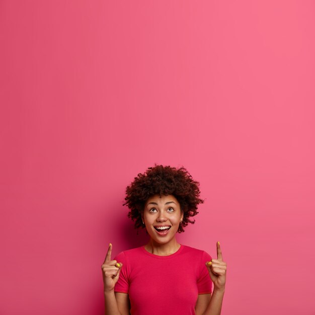 Jovem afro-americana sorridente e positiva aponta o dedo indicador para cima