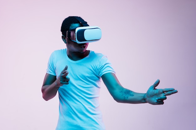 Jovem afro-americano apontando e usando óculos VR em luz de néon em fundo gradiente