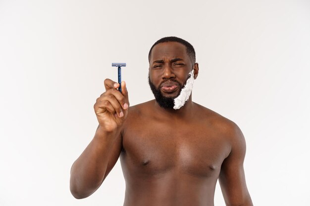 Jovem afro-americano barbeando-se na higiene pessoal da rotina matinal do banheiro no conceito matinal