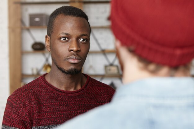Jovem afro-americano bonito com um suéter casual em pé no interior de um café moderno