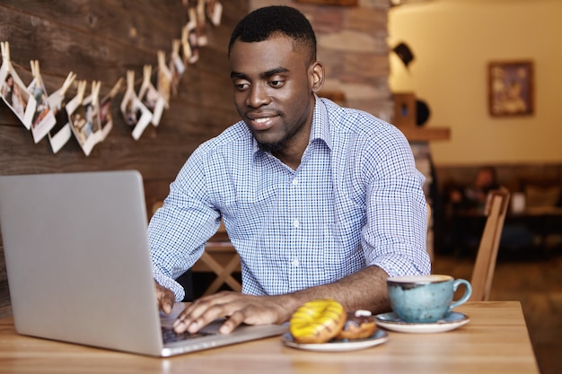 Jovem afro-americano confiante, trabalhador de escritório com roupa formal, digitando em um laptop