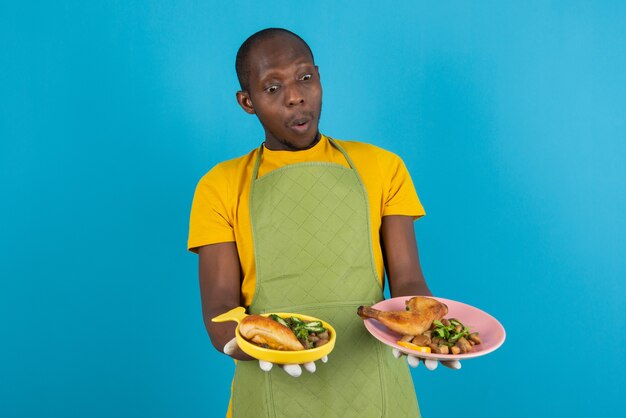 Jovem afro-americano de avental segurando frango frito na parede azul
