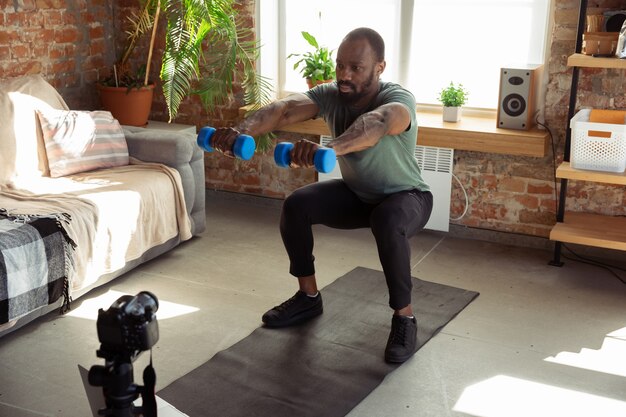 Jovem afro-americano, ensinando em casa cursos on-line de fitness, estilo de vida aeróbico e esportivo durante a quarentena, gravação na câmera, streaming