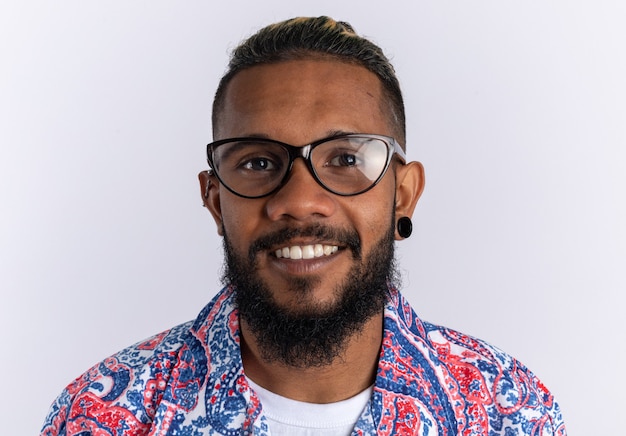 Jovem afro-americano feliz com uma camisa colorida de óculos, olhando para a câmera, sorrindo alegremente