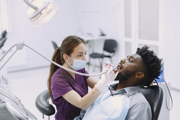 Jovem afro-americano. Indivíduo em visita ao consultório dentário para prevenção da cavidade oral. Homem e médico famoso durante o exame de dentes.