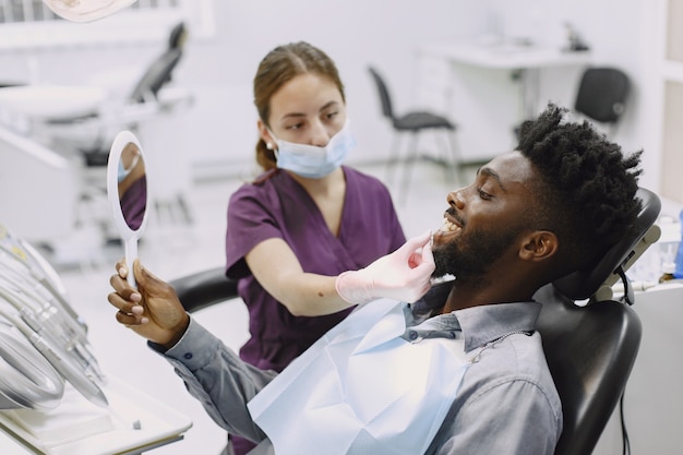 Jovem afro-americano. Indivíduo em visita ao consultório dentário para prevenção da cavidade oral. Homem e médico famoso durante o exame de dentes.