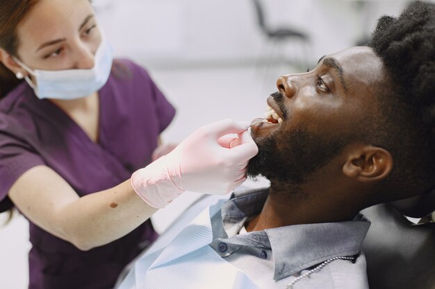 Jovem afro-americano. Indivíduo em visita ao consultório dentário para prevenção da cavidade oral. Homem e médico famoso durante o exame de dentes.