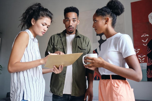 Foto grátis jovem afro-americano olhando espantado para a câmera durante o trabalho com colegas no espaço de coworking moderno