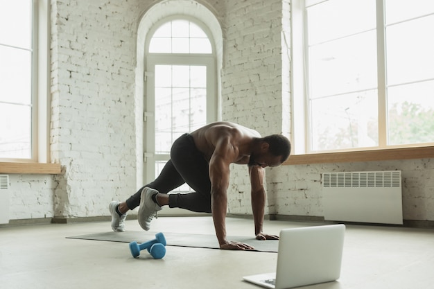 Jovem afro-americano treinando em casa, fazendo exercícios de fitness, aeróbica