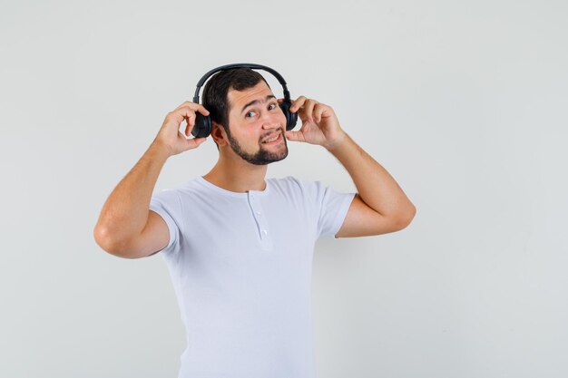 Jovem ajustando fones de ouvido em t-shirt branca e olhando feliz. vista frontal.