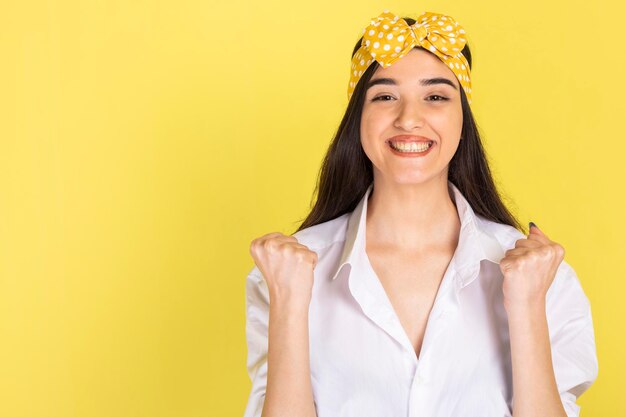 Jovem alegre apertando os punhos e sorrindo em fundo amarelo Foto de alta qualidade