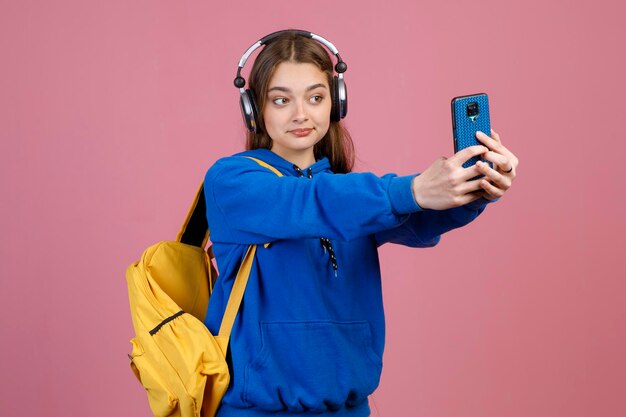 Jovem alegre com fones de ouvido tomando selfie com smartphone e sorrindo