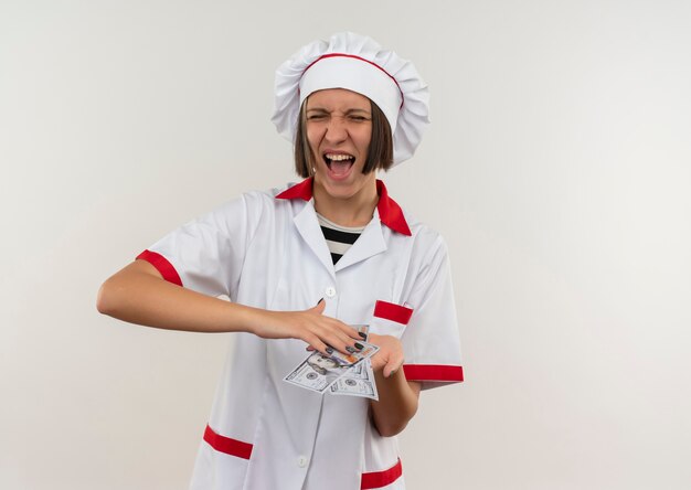 Jovem alegre cozinheira com uniforme de chef segurando dinheiro isolado no branco