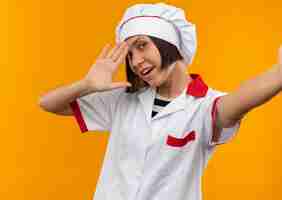 Foto grátis jovem alegre cozinheira em uniforme de chef, estendendo a mão e gesticulando 