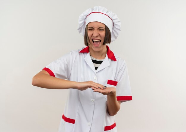 Jovem alegre cozinheira em uniforme de chef, mantendo as mãos juntas com os olhos fechados, isolados no branco