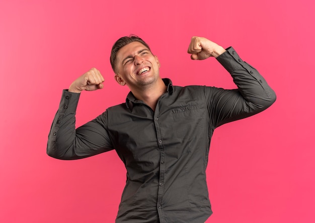 Foto grátis jovem alegre e alegre homem bonito tensiona os bíceps, olhando para cima, isolado no espaço rosa com espaço de cópia